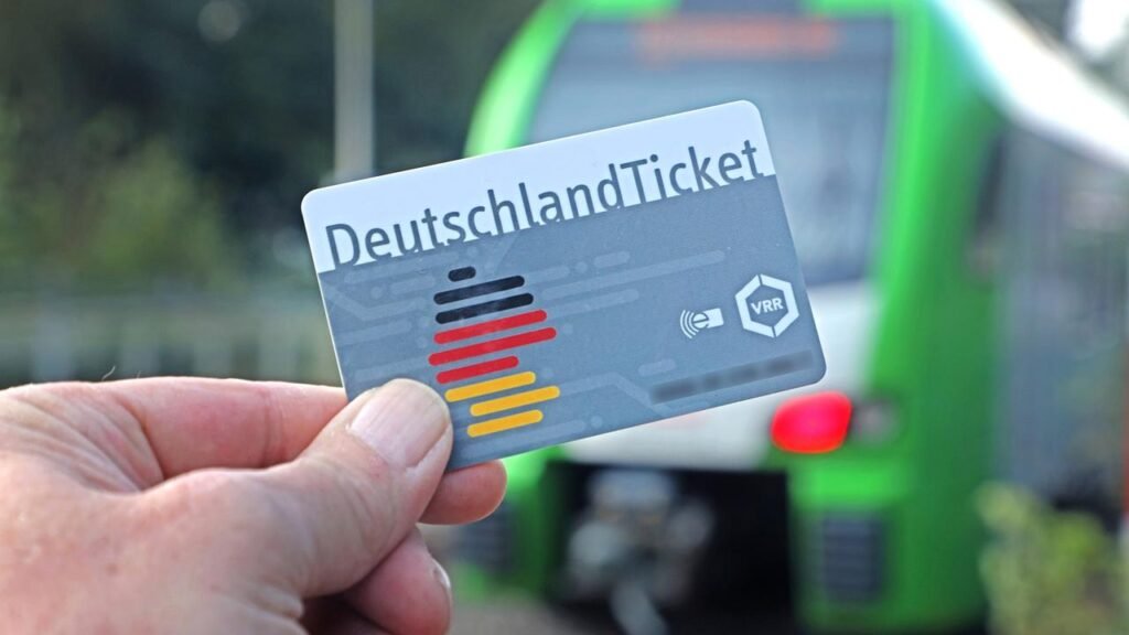Ръка държи карта Deutschlandticket пред зелен регионален влак